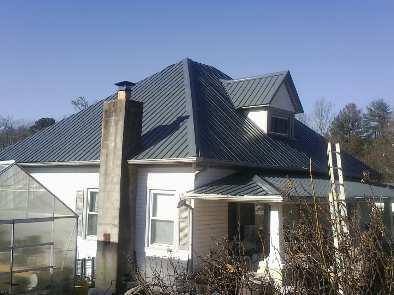 Dark blue standing seam metal roof on a white farmhouse with dormer — Slate & Tile Roof Repair by Roofing Brothers in Parshall