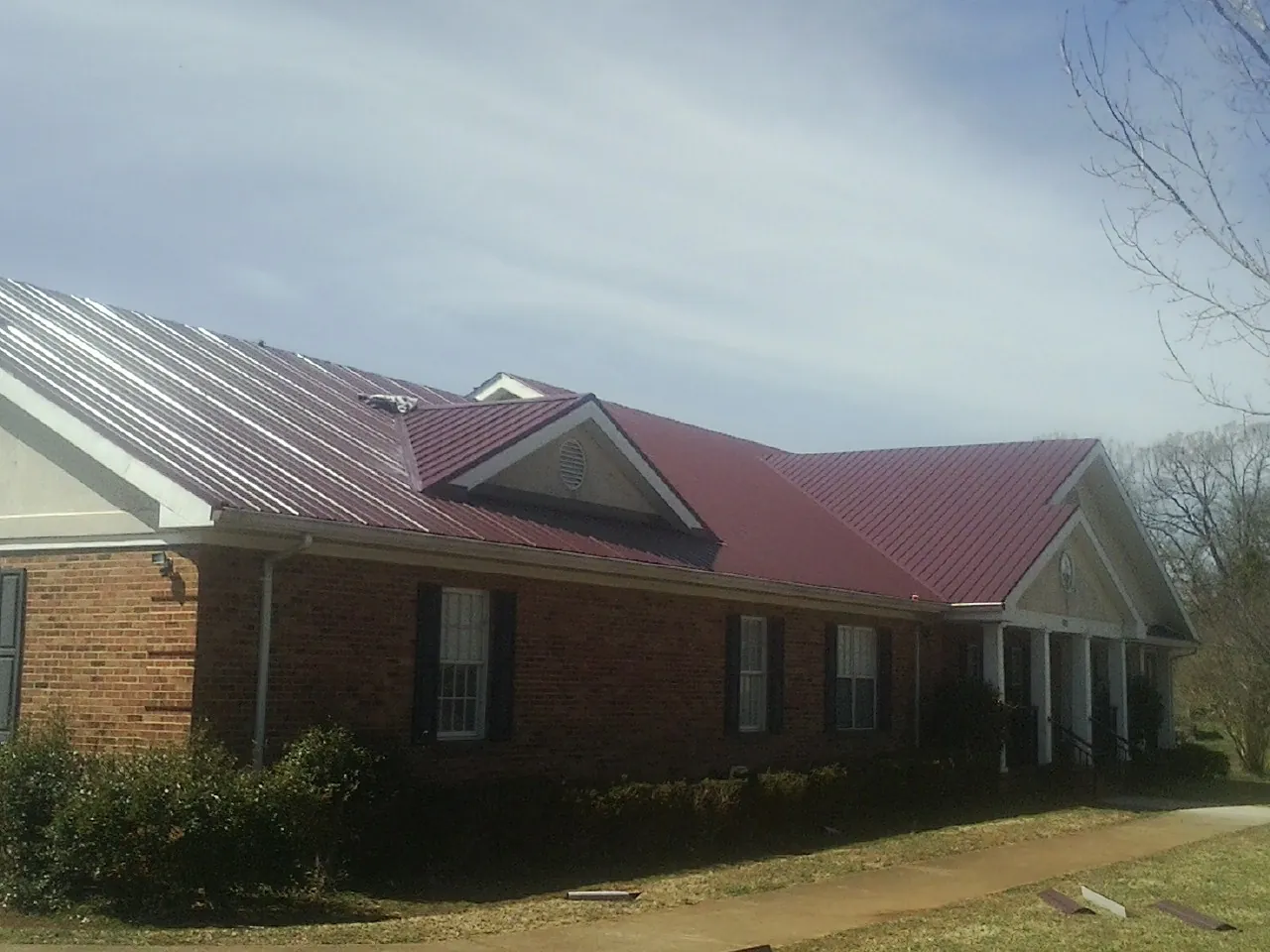Red metal roof with gabled entries on a long brick building, from a Hail Damage Roof Repair job in Parshall