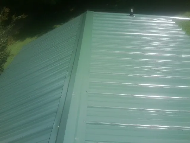 New green metal panels meeting at the ridge of a roof — Flat Roof Repair work by our crew in Parshall