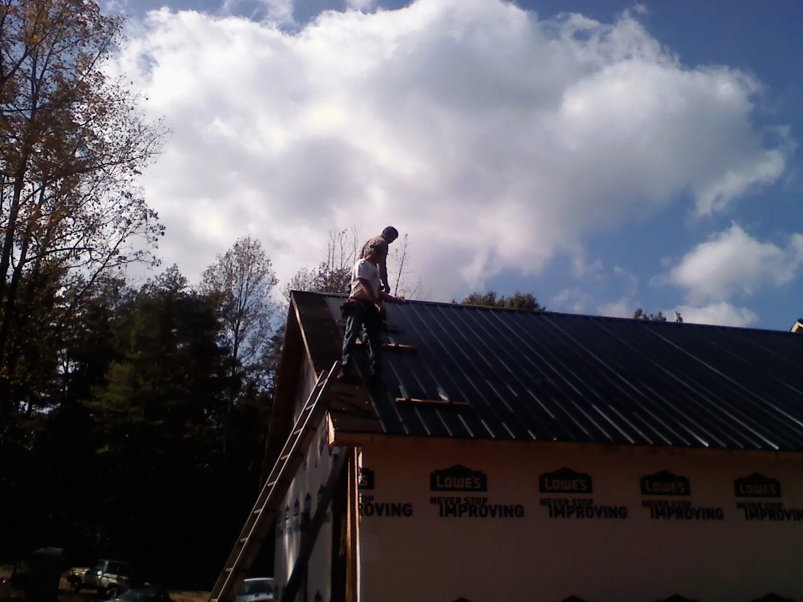 Roofer fastening dark metal panels high against a cloudy sky, from a Roof Inspection job in Parshall