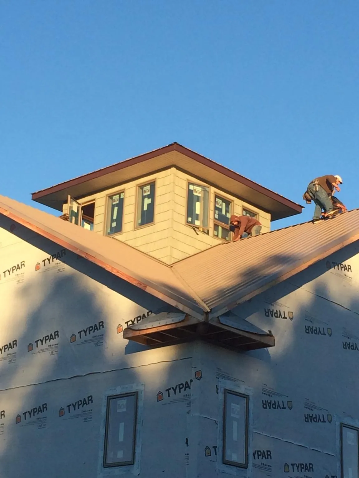 Roofers working around a rooftop cupola on a new metal roof at sunset — Roof Waterproofing in Parshall by Roofing Brothers